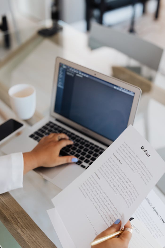 A person reviewing a contract on a laptop in a modern office setting.